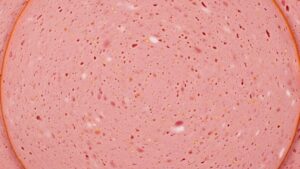 Cross-section of bologna showing smooth pink texture and fine emulsification of meat with visible spices throughout the processed deli meat